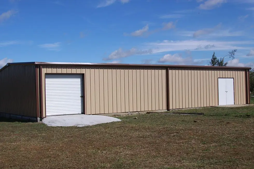 Finished tan metal commercial building with a white roll-up door and a white personnel door, under open sky in Decatur, Alabama