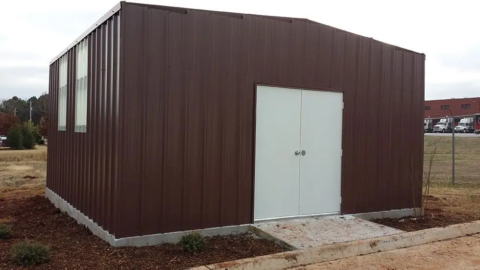 Completed brown-panel metal building with double white doors and landscaped beds, photographed after a Hall Construction handover